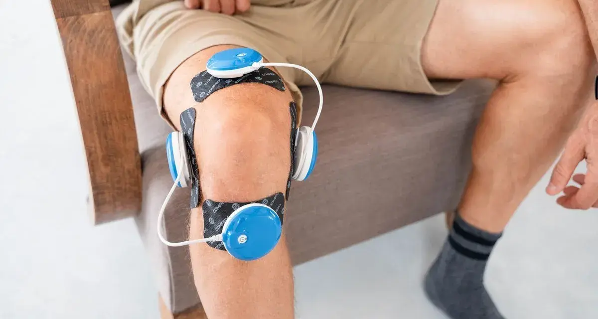 Un homme utilise un appareil d'électrostimulation pour son genou, une solution pour le traitement de la tendinite du genou.