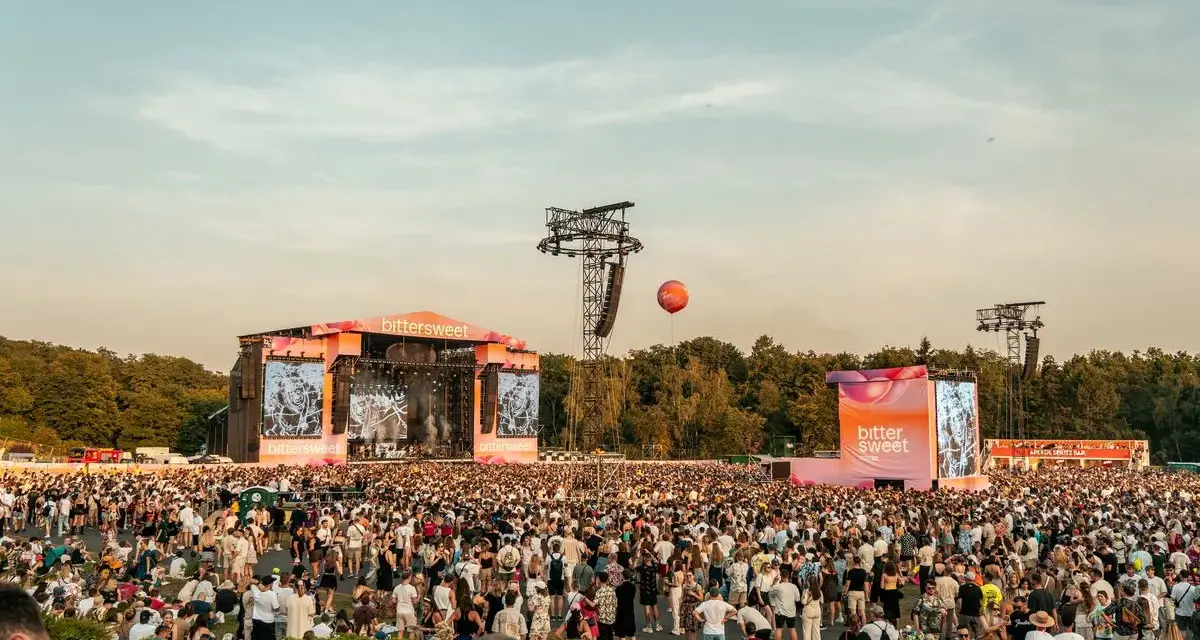 Tłum ludzi na festiwalu bittersweet, dwie sceny, ekrany z grafikami i pomarańczowy balon na niebie.