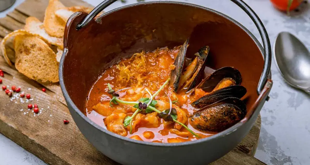 Un delicioso suquet de peix, con mejillones y gambas en una cazuela de barro, acompañado de tostadas.