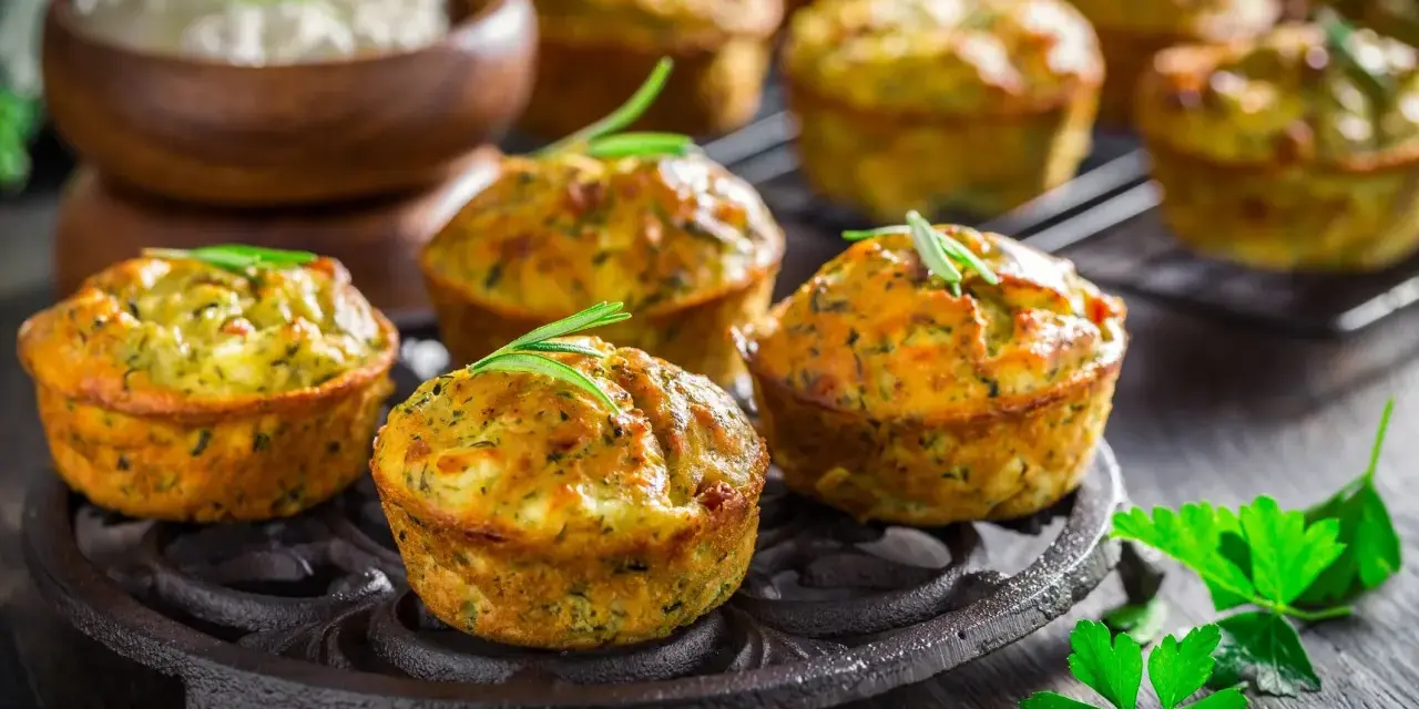 Deliziosi tortini di zucchine dorati, guarniti con rosmarino, su un piatto di ghisa. Sullo sfondo, una ciotola di formaggio fresco.