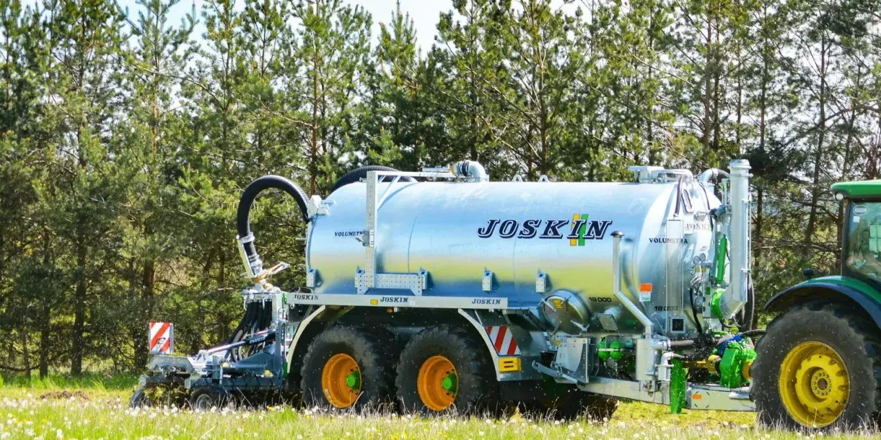 Cysterna JOSKIN na polu, gotowa do rozrzucenia gnojowicy lub gnojówki. Zielony traktor czeka w tle.
