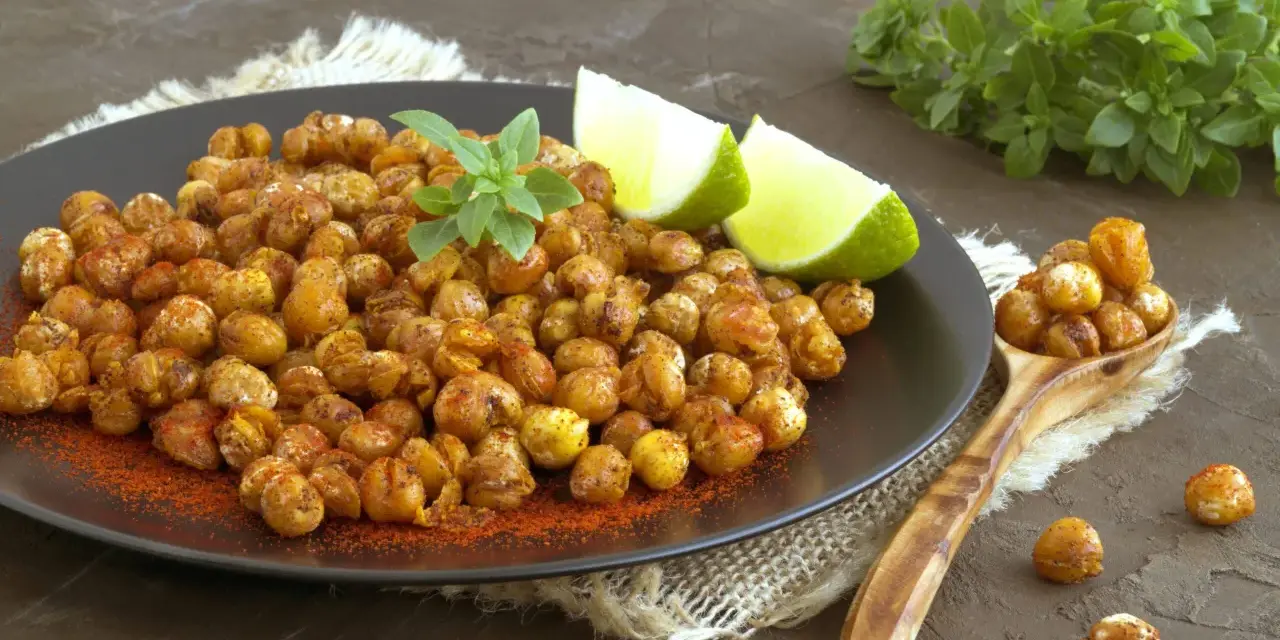 Ceci croccanti al forno, conditi con paprika e guarniti con basilico fresco e spicchi di lime, invitano a uno snack salutare e gustoso.