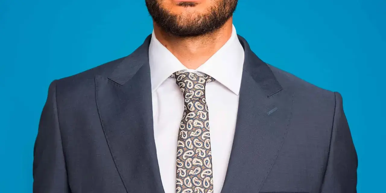Uomo con abito blu, camicia bianca e cravatta fantasia. Un abbinamento classico per un look elegante.