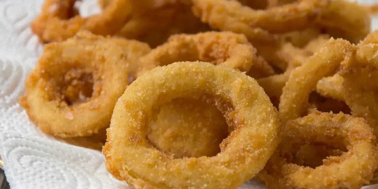 Knusprige zwiebelringe in der pfanne, goldbraun und perfekt frittiert, liegen auf einem weißen Küchentuch.