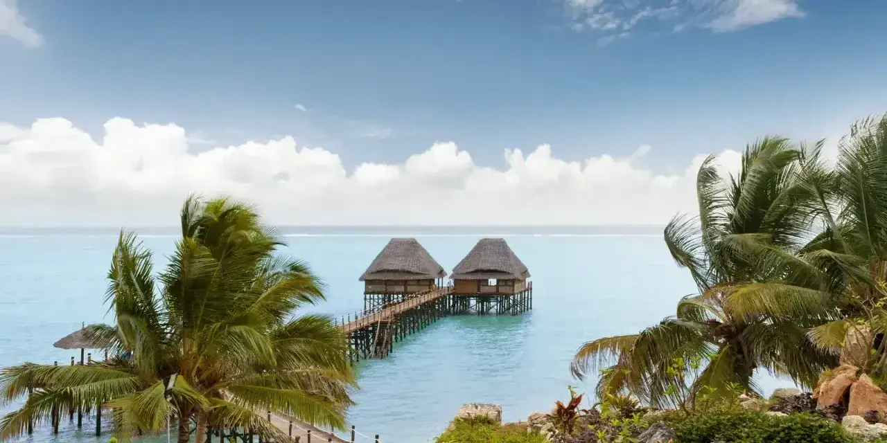 Dwa domki na wodzie z palmami w tle, idealne na spokojny wypoczynek podczas pory deszczowej na Zanzibarze.