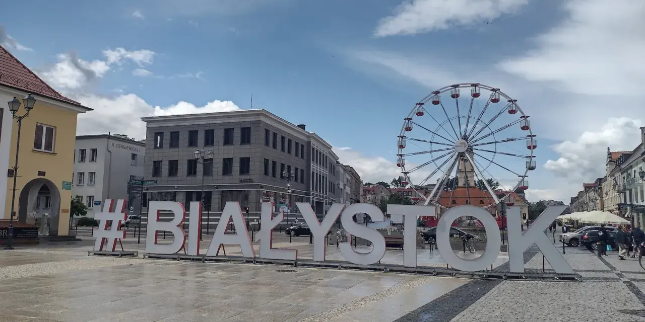 #Białystok - wielki napis zaprasza do odkrywania atrakcji miasta, w tle koło widokowe i zabytkowa zabudowa.