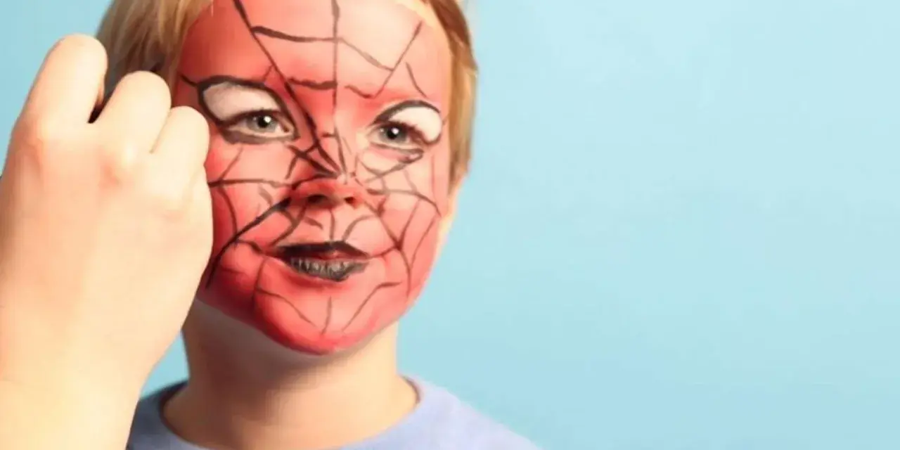 Ein Kind wird mit einem Spiderman-Gesicht bemalt. Rote Farbe und schwarze Spinnennetzmuster verwandeln das Gesicht in eine Superheldenmaske.