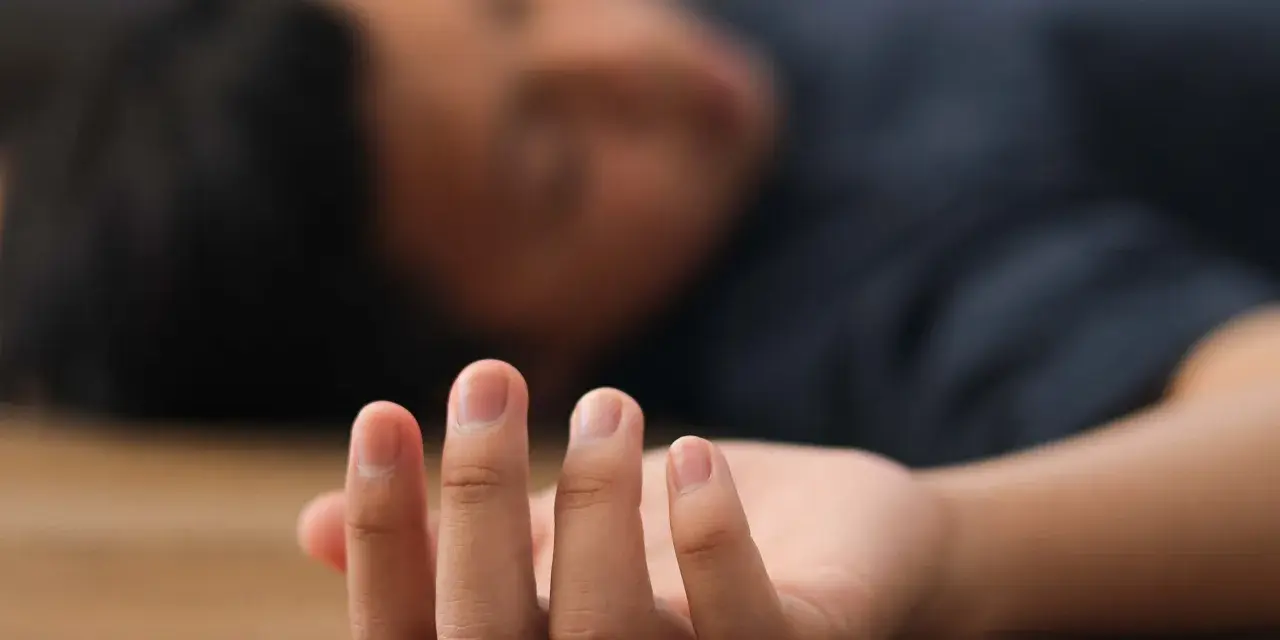 Nahaufnahme einer Hand, die auf dem Boden liegt, während eine Person mit einem epileptischen Anfall bewusstlos ist.