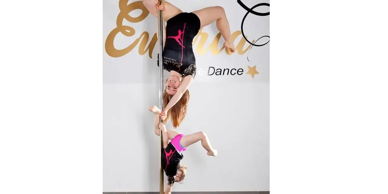 Dwie tancerki, dorosła i dziecko, wykonują akrobacje na słupie. To dowód, że pole dance dla dzieci to świetna zabawa i aktywność.