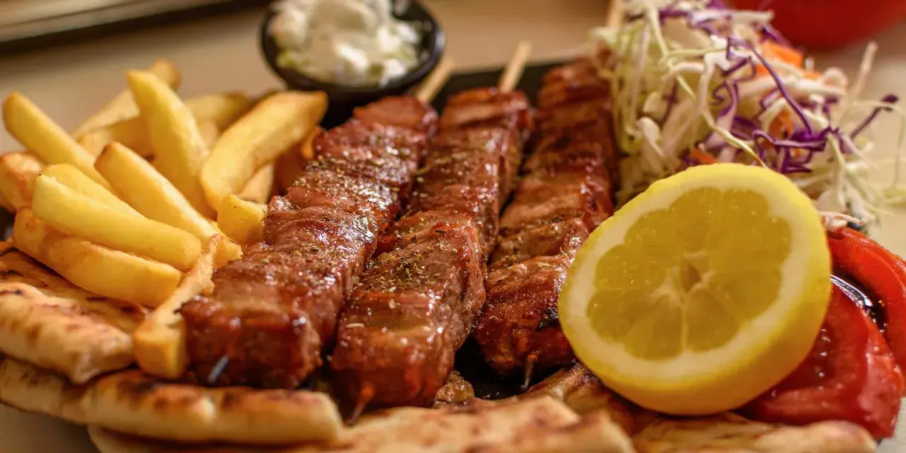 Pyszne souvlaki na patykach, podane z frytkami, pitą, surówką i cytryną.