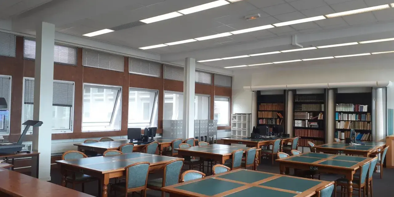 Salle de lecture avec tables, chaises et étagères de livres.