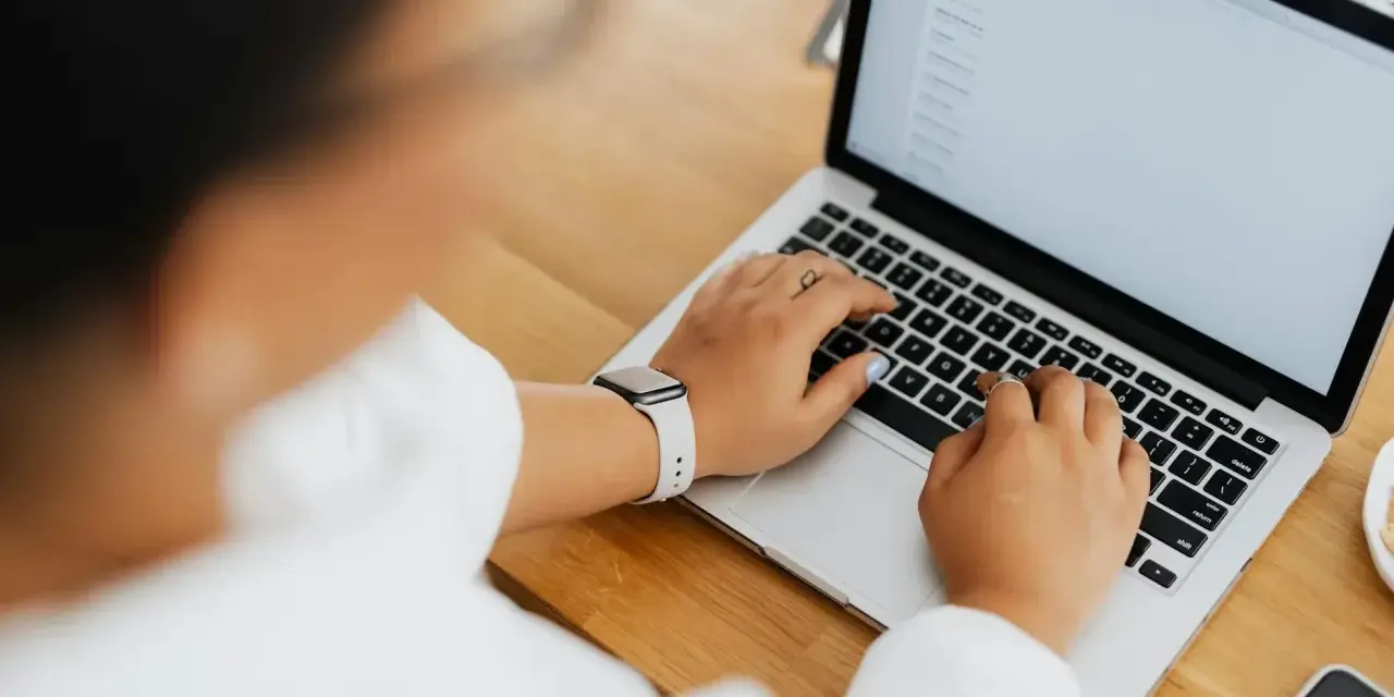 Kobieta pisze na laptopie, na ekranie widać artykuł po niemiecku.