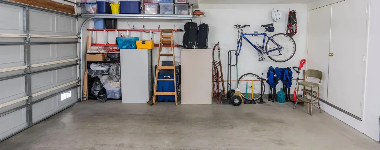 Garage med cykel, stegar, förvaringslådor och en liten fönsterlucka för ventilation.