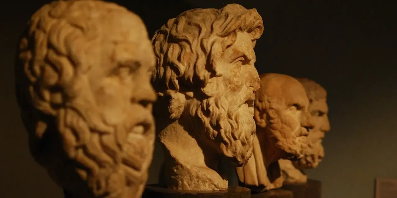Bustos de mármol de filósofos de la edad antigua Grecia, con barbas y miradas serias, alineados en un museo.