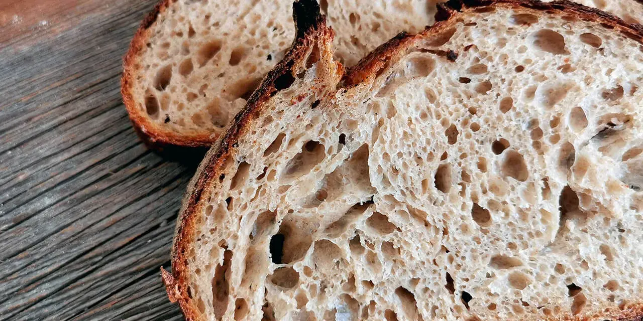 Zwei Scheiben rustikales Sauerteigbrot mit großer Porung liegen auf einem Holzbrett. Die Sauerteig Vorteile sind offensichtlich: ein toller Geschmack und eine bekömmliche Textur.
