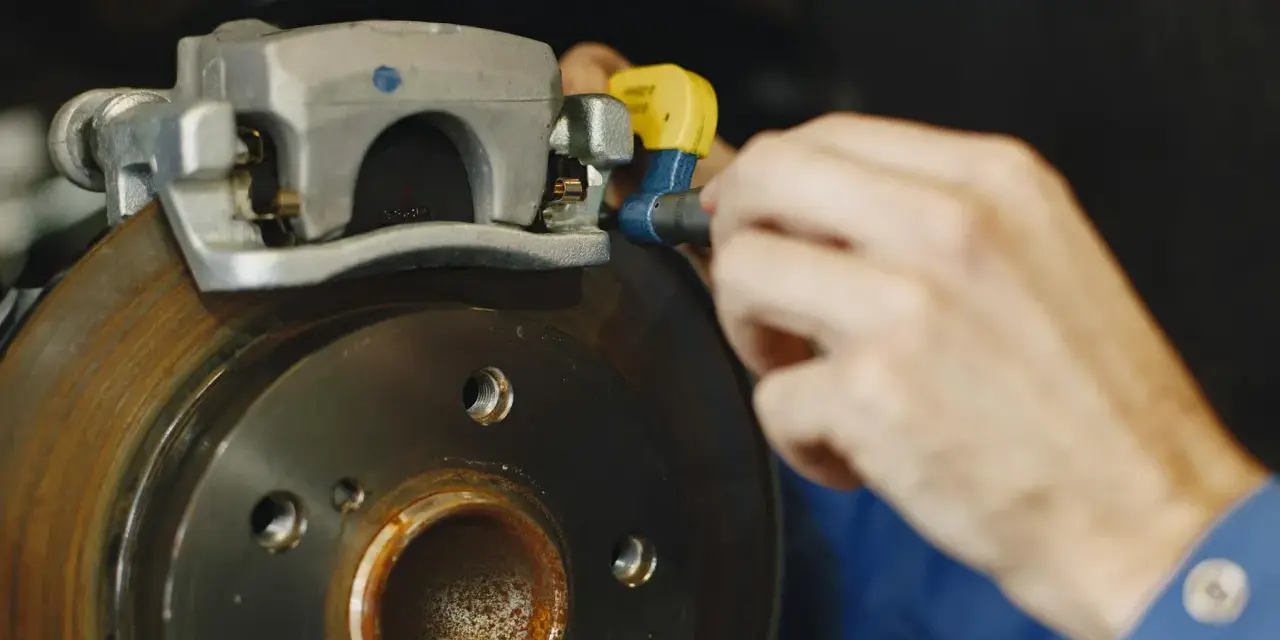 Mechanik dokręca śrubę w jarzmie zacisku hamulcowego, naprawiając układ hamulcowy pojazdu.