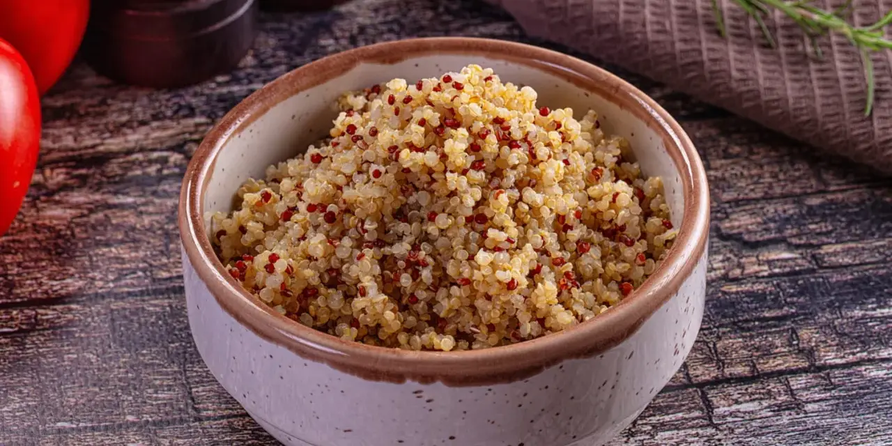 Un bol de quinoa, riche en fibres, prêt à être dégusté. Des tomates rouges et une branche de romarin complètent la scène.