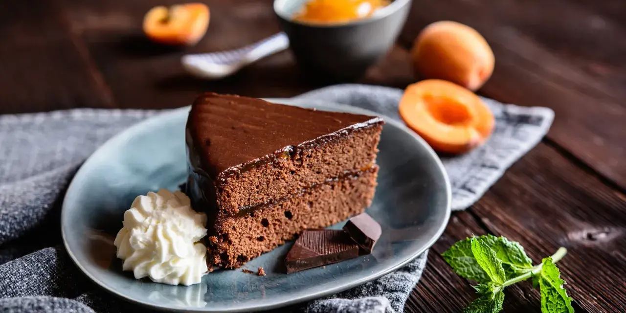 Ein Stück Sachertorte, das aussieht wie vom Original Sachertorte Rezept, mit Schlagobers, Schokolade und Marillenmarmelade.