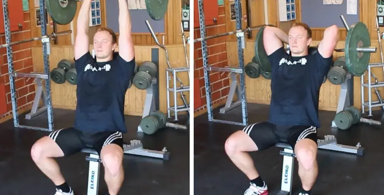 Man utför french press i gym. Han sitter på en bänk med en skivstång över huvudet, redo att sänka den bakom nacken.