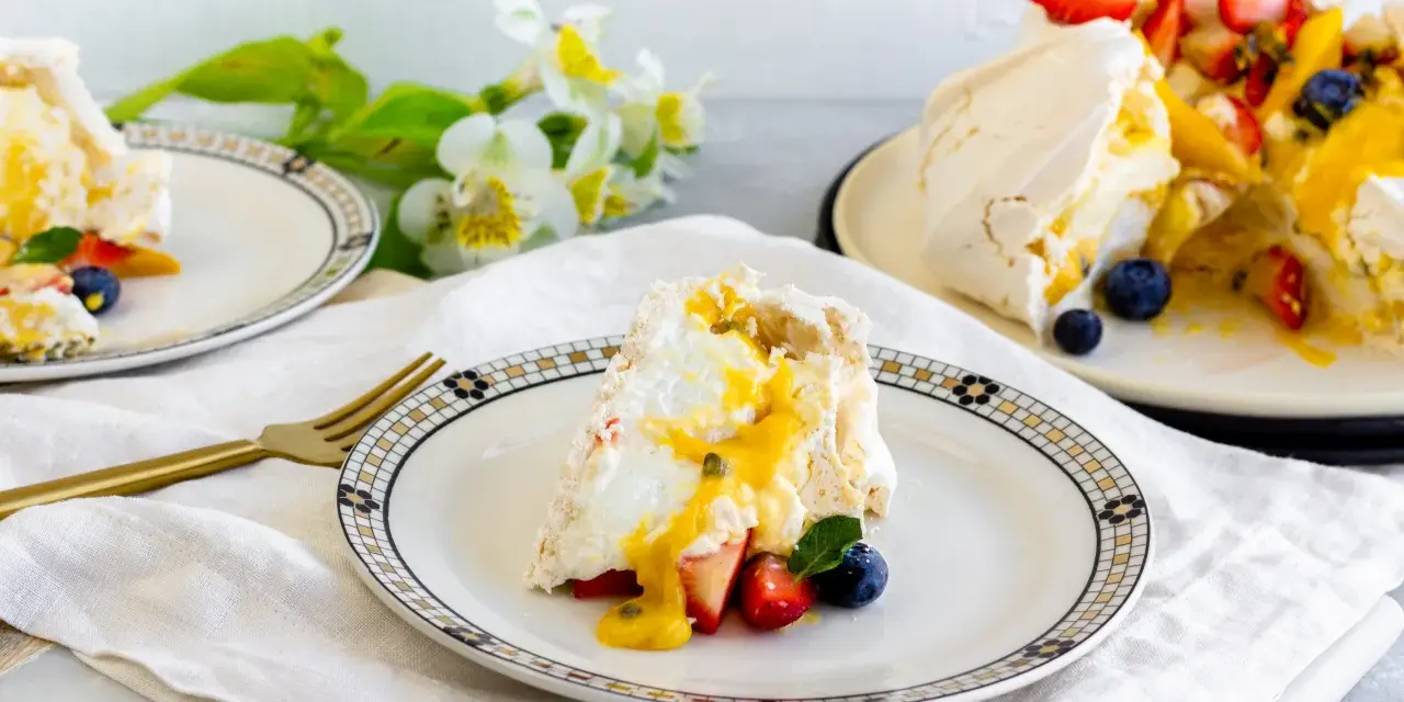 Porción de pavlova con fresas, arándanos y mango, bañada en salsa de maracuyá. Los pavlova ingredientes son visibles en este postre.