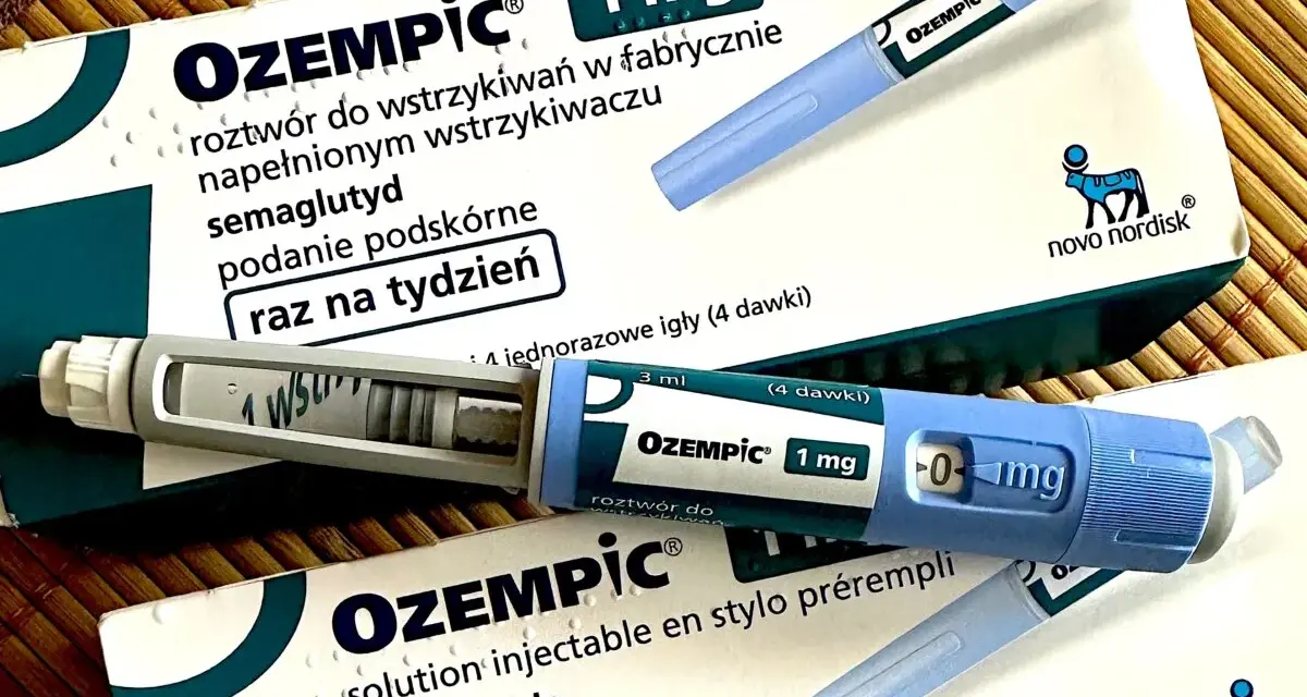 Dwa opakowania i dwa peny leku Ozempic 1 mg na podkładce bambusowej.