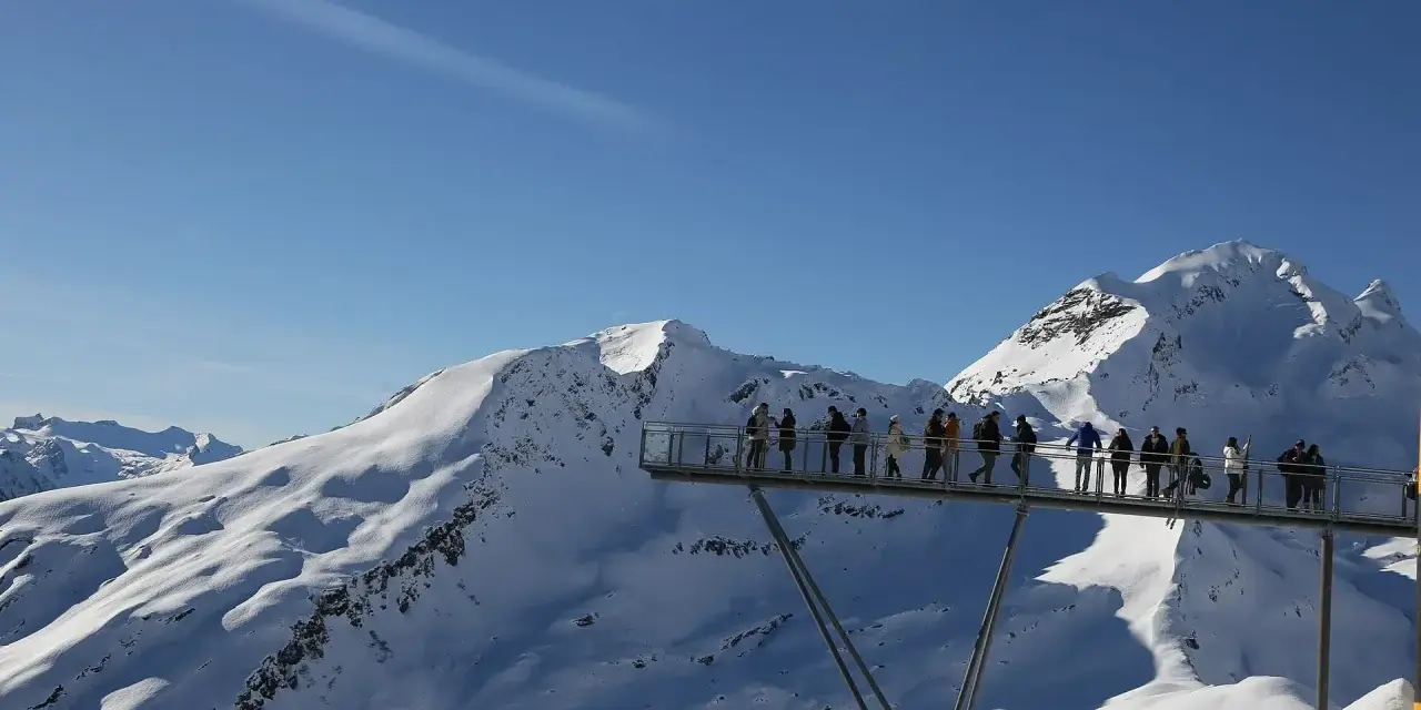 Ludzie na platformie widokowej podziwiają ośnieżone szczyty Alp, jakby byli w świecie Grindelwalda.