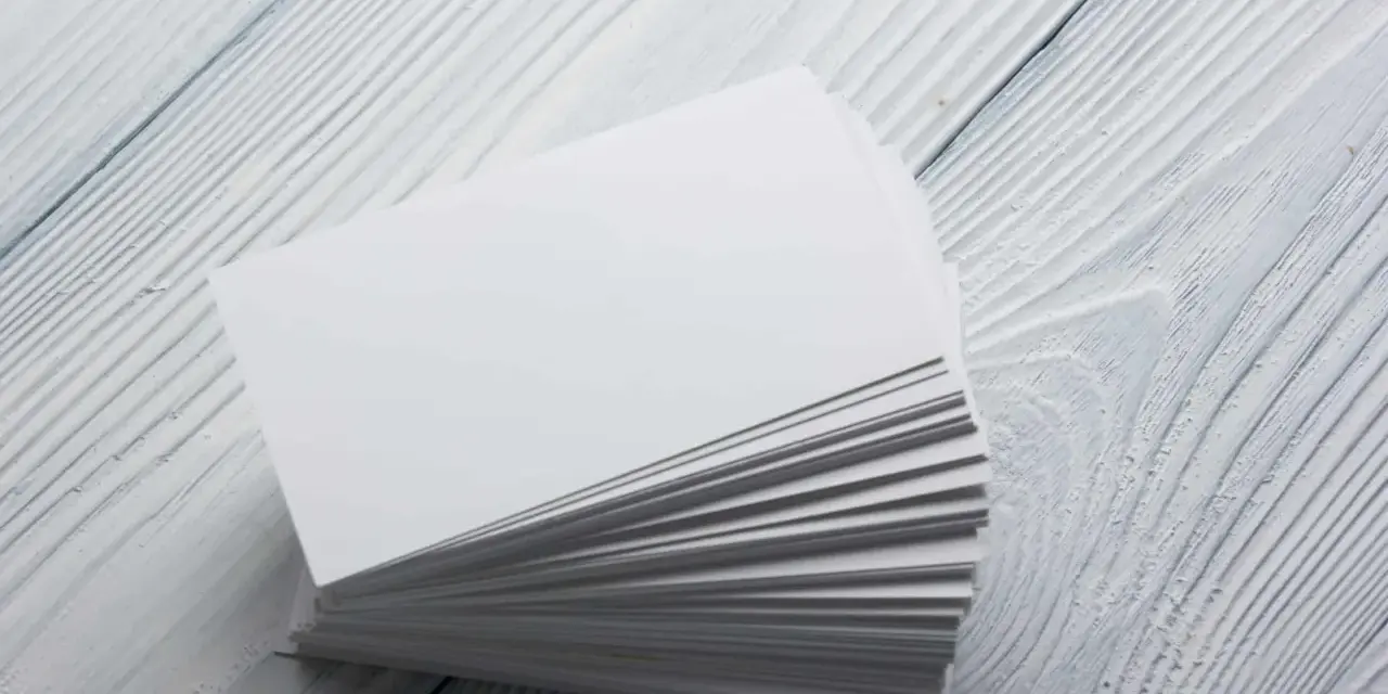 Stos białych wizytówek, idealnych na papier satynowy lub kredowy, leży na drewnianym blacie.