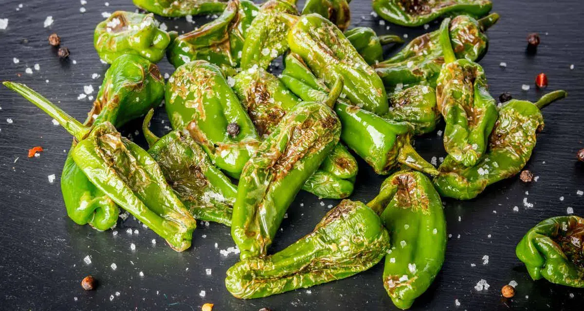 Friggitelli verdi, cotti in friggitrice ad aria, cosparsi di sale grosso e pepe nero su una superficie scura.