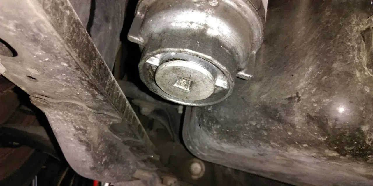 Filtre à huile de voiture sous le véhicule, avec une clé carrée insérée.
