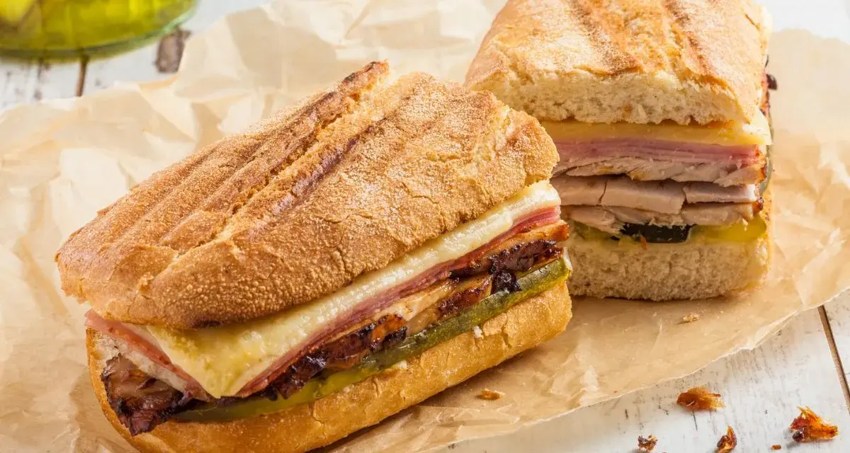 Dos sándwiches cubanos a la parrilla con capas de carne, queso derretido y pepinillos.