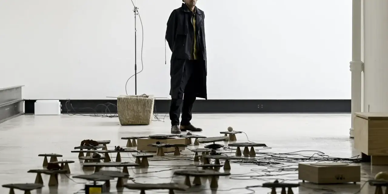 Tarek Atoui, artiste, se tient au milieu d'une installation sonore avec de nombreuses petites structures en pierre et en bois reliées par des câbles.