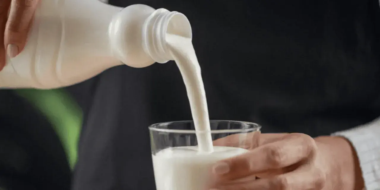 Kefir, naturalny probiotyk, pomaga zwalczać grzybicę jamy ustnej. Biały napój leje się z butelki do szklanki.