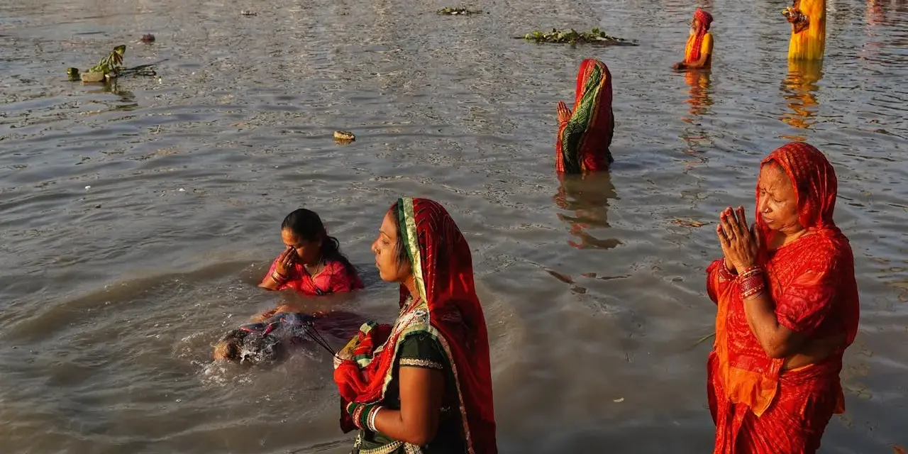 Mujeres rezan en el río Ganges, con vestimentas coloridas y el agua hasta la cintura.