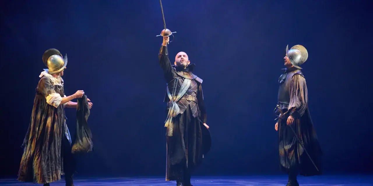 Tres hombres con armadura y espadas en un escenario. El del centro levanta su espada. Escena de "El alcalde de Zalamea".