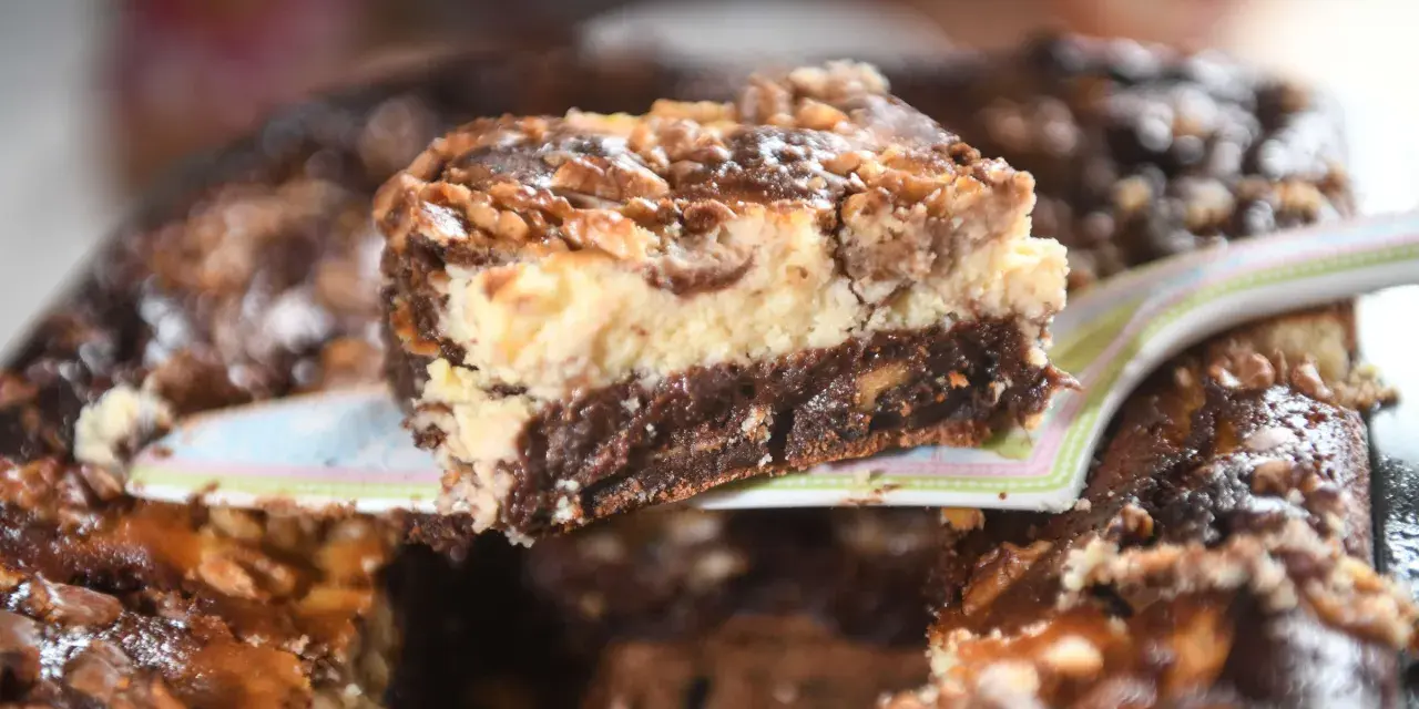Ein Stück saftiger "friss dich dumm kuchen vom blech" mit Schichten aus Schokolade, Käsekuchen und Nüssen wird serviert.