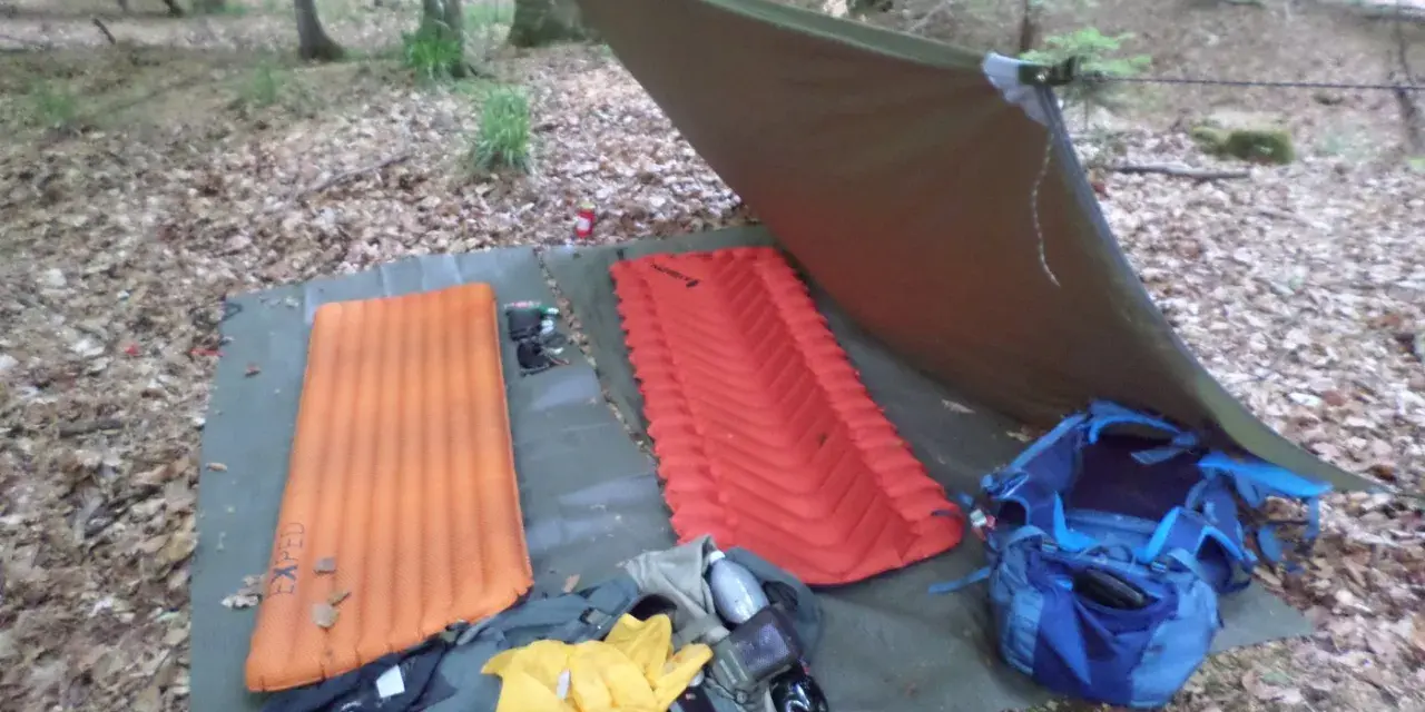 Zwei Isomatten, ein Tarp und Rucksäcke liegen bereit, um unter freiem Himmel zu schlafen.