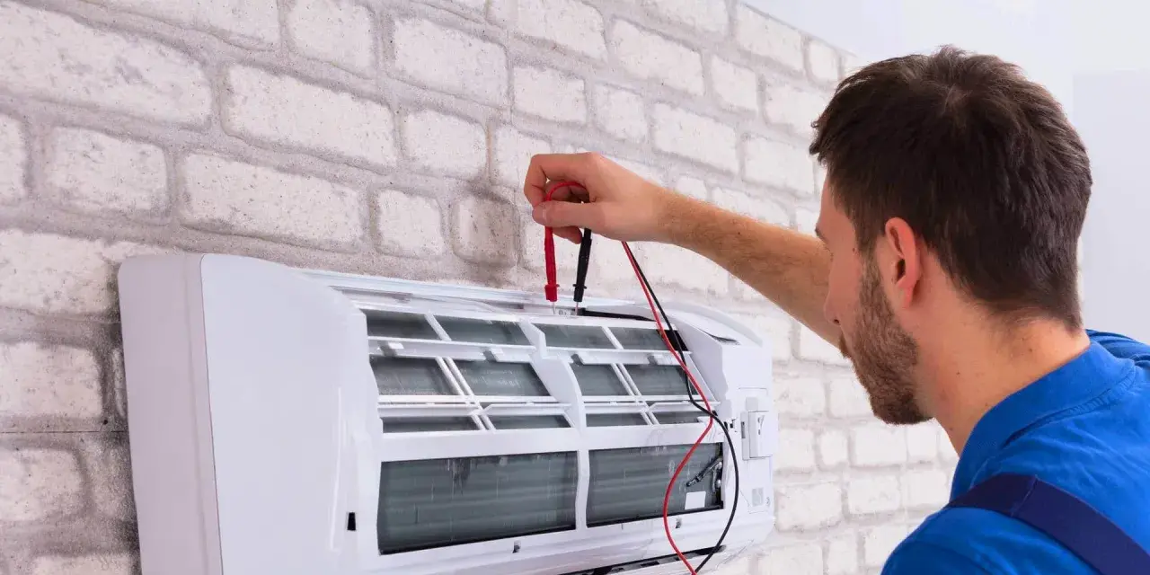 Sprawdź, jaka jest odgrzybianie klimatyzacji cena. Technik z miernikiem przy białej klimatyzacji.