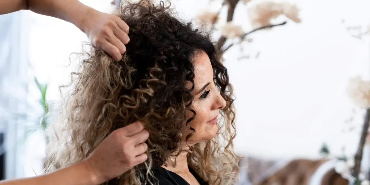 Stylista układa kręcone włosy klientki, przygotowując się do strzyżenia. Wskazówki, jak obciąć kręcone włosy, pomogą uzyskać idealny kształt.