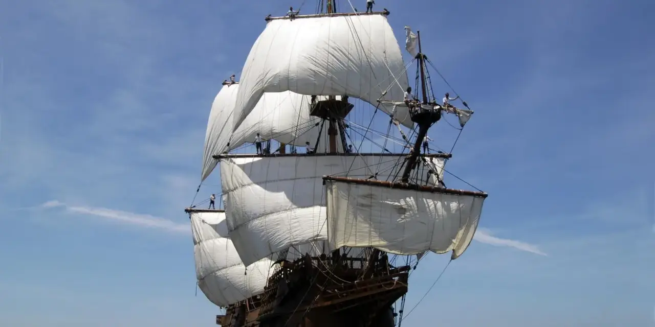 Un majestueux galion espagnol navigue sous un ciel bleu, ses voiles blanches gonflées par le vent.