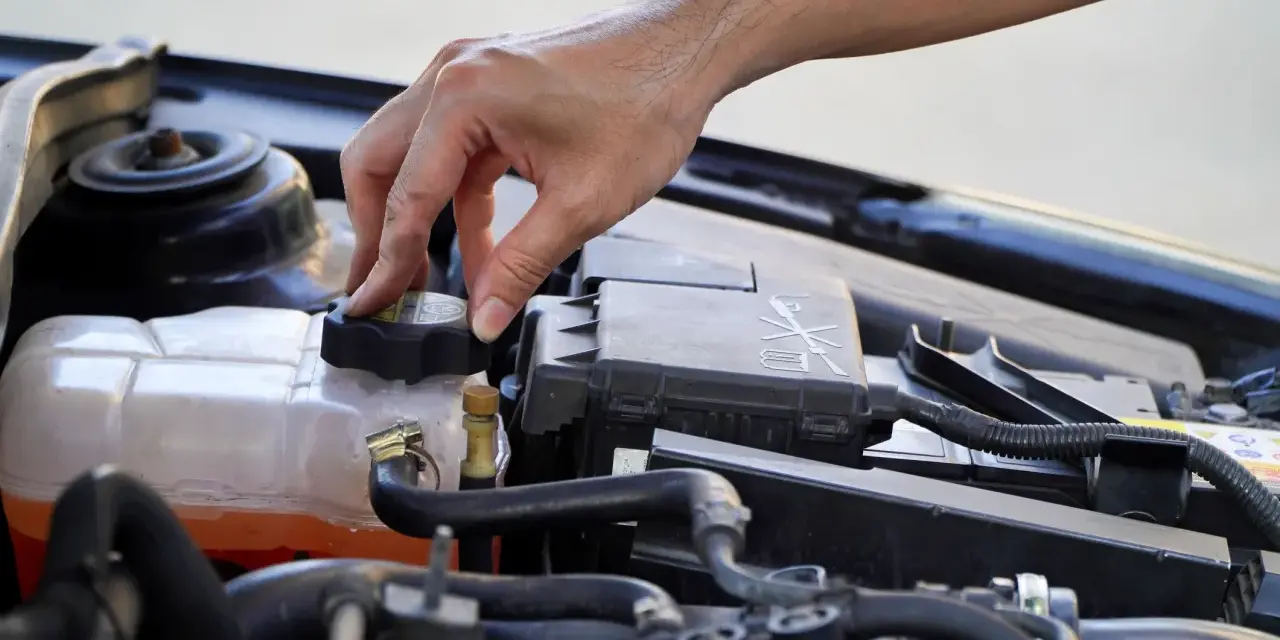 A hand twists the cap on a car's coolant reservoir, a step in learning how to dispose of antifreeze safely.