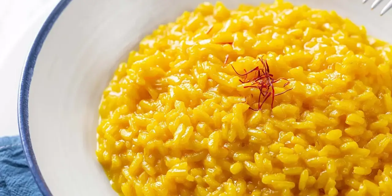 Un cremoso risotto alla milanese, giallo intenso grazie allo zafferano, guarnito con fili rossi.