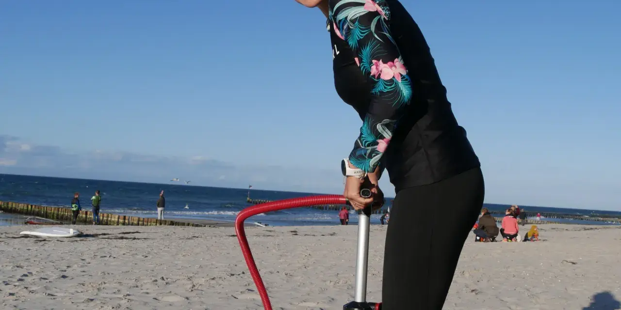 Frau pumpt SUP auf. Am Strand bereitet sie sich auf Wassersport vor.