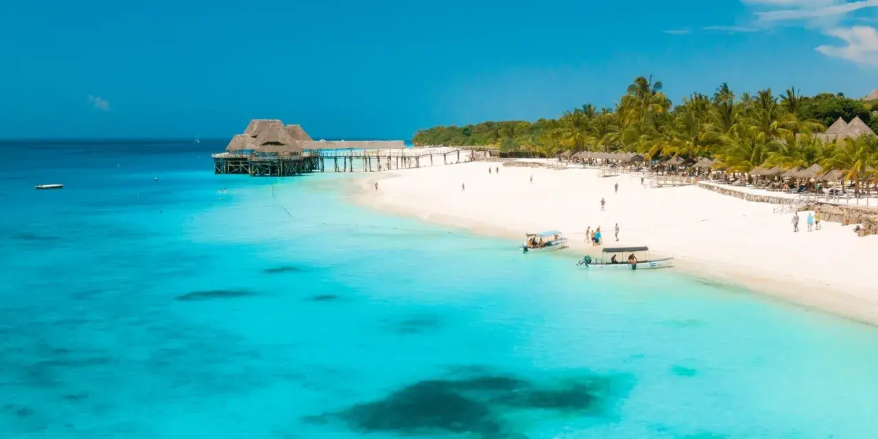 Rajskie plaże Zanzibaru w lutym. Turkusowa woda, biały piasek, palmy i urokliwy pomost z domkami na wodzie.