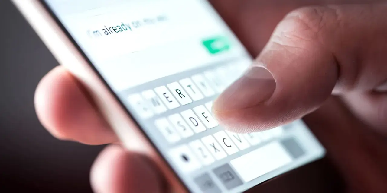 Palec pisze na klawiaturze telefonu: "Już w drodze na wesele!". Potwierdzenie przybycia na wesele sms.
