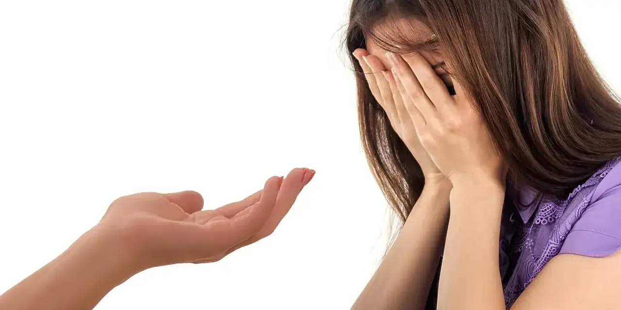 Kobieta płacze, zakrywając twarz dłońmi. Wyciągnięta dłoń oferuje wsparcie, symbolizując trudny moment, jak przyznać się do kłamstwa.