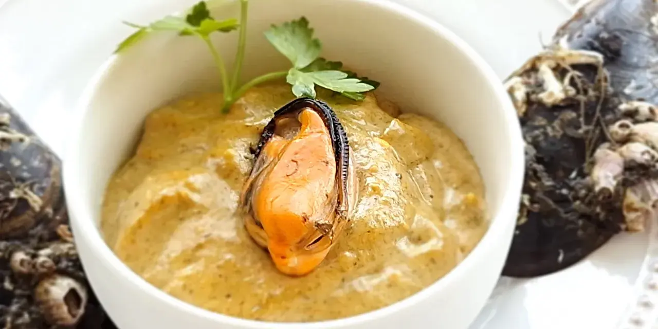 Paté de mejillones cremoso en cuenco blanco, decorado con perejil y mejillones enteros al lado.