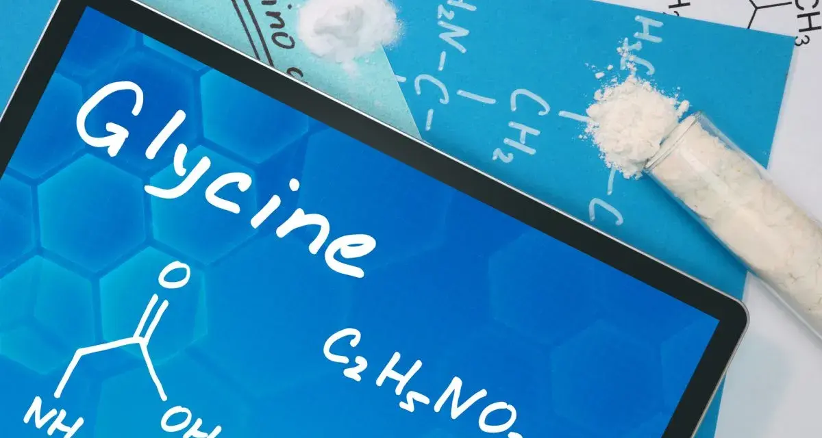 Tablet z napisem "Glycine", wzorem chemicznym i próbówką z proszkiem. Informacje o glicynie i jej dawkowanie.