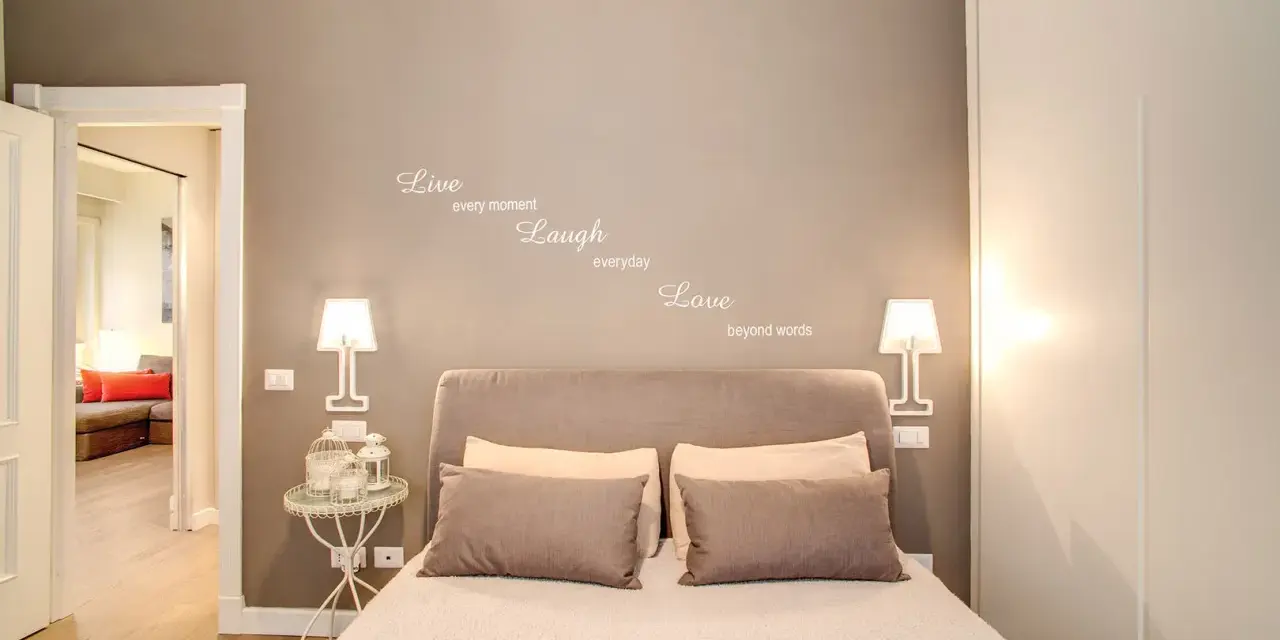 Camere da letto belle con citazione "Live, Laugh, Love" sulla parete. Letto accogliente con cuscini e lampade moderne.