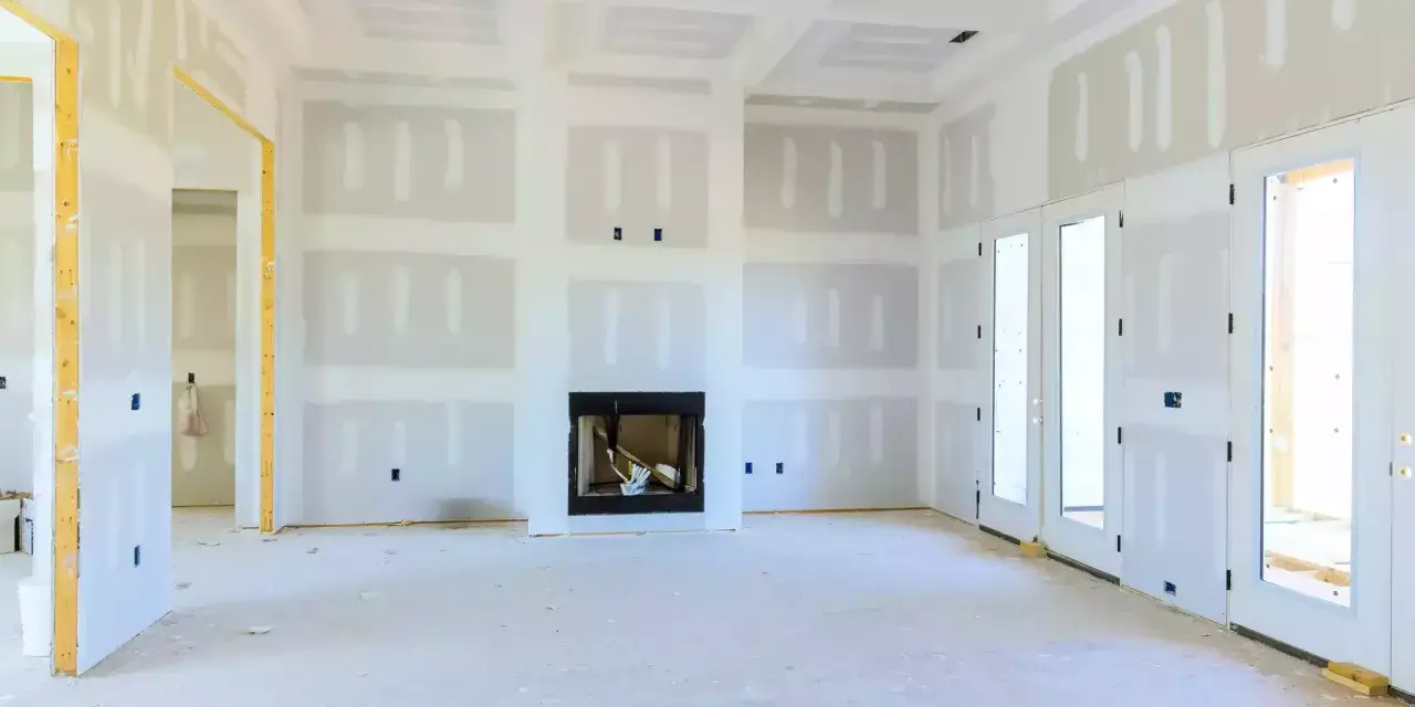 Interno di una casa in costruzione con pareti e soffitto in cartongesso, camino e porte a doppio battente.