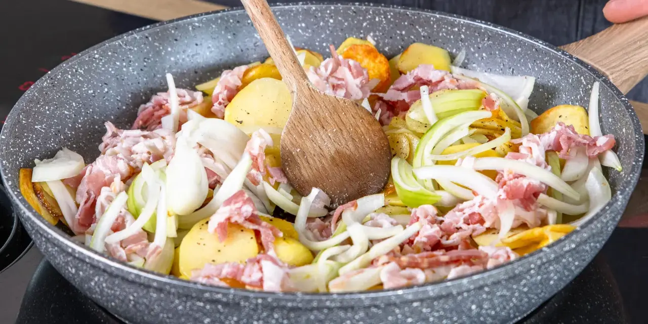 Zutaten für einen herzhaften Hamburger Pannfisch werden in einer Pfanne vermischt: Kartoffeln, Speck und Zwiebeln.